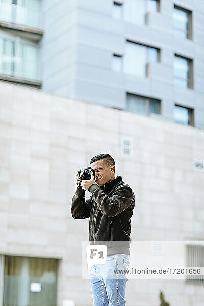 Junge männliche Fachkraft  die durch die Kamera fotografiert  während sie vor einem Gebäude steht