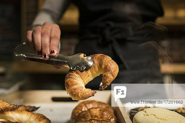 Junger Bäcker hält Croissant in einer Servierzange in einer Bäckerei