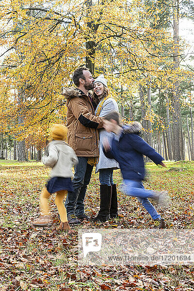 Man kissing woman while standing with children playing around in forest