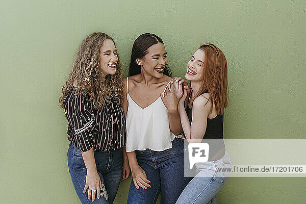 Fröhliche junge Freundinnen stehen an einer grünen Wand