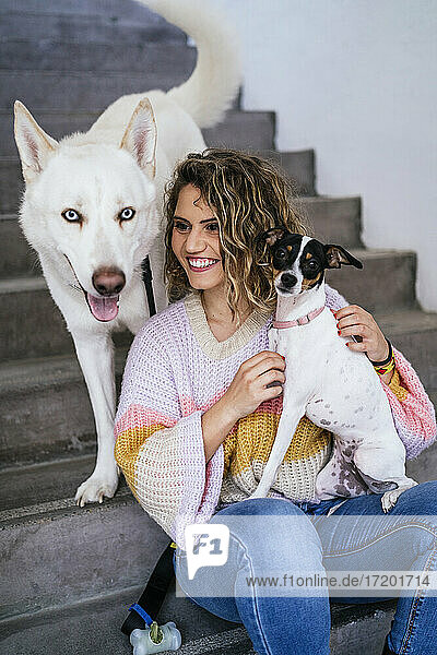 Lächelnde Frau schaut weg  während sie einen Jack Russell Terrier gegen einen Siberian Husky auf einer Treppe hält