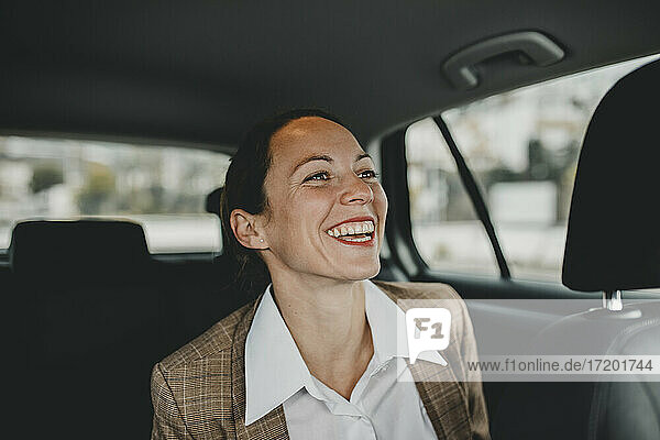 Fröhliche weibliche Fachkraft sitzt auf dem Rücksitz während der Fahrt im Taxi