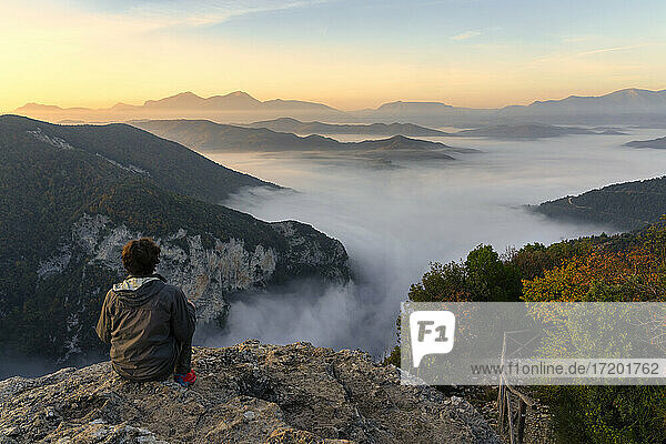 Männlicher Tourist sitzt auf einer Klippe und beobachtet den Sonnenaufgang in der Furlo-Schlucht  Marken  Italien