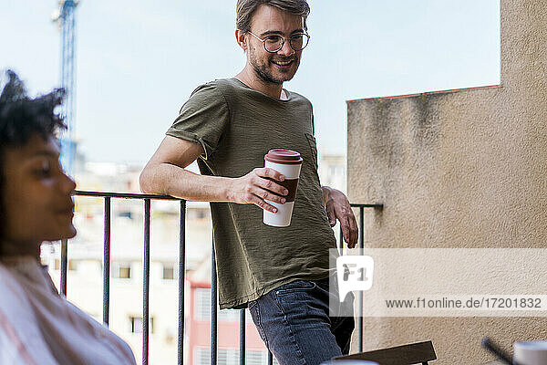 Young male entrepreneur with reusable cup leaning on railing during coffee break at office