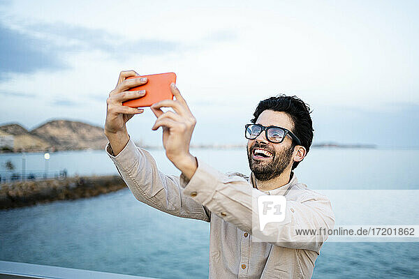 Cheerful businessman taking selfie through mobile phone at the sea
