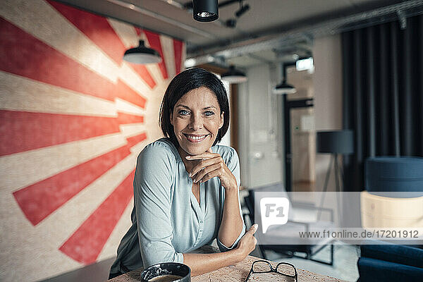 Lächelnde Geschäftsfrau  die sich im Büro auf einen Tisch stützt