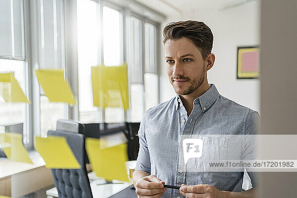 Confident businessman brainstorming while looking at adhesive notes at office