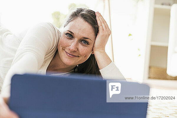 Lächelnde Frau mit digitalem Tablet im Wohnzimmer liegend