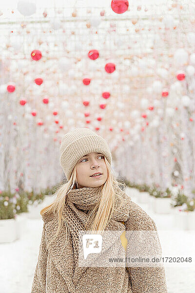 Thoughtful teenage girl wearing warm clothing while standing under decoration