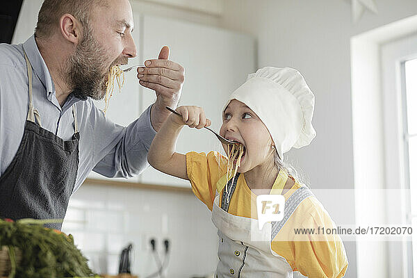 Father and daughter eating food while standing in kitchen at home