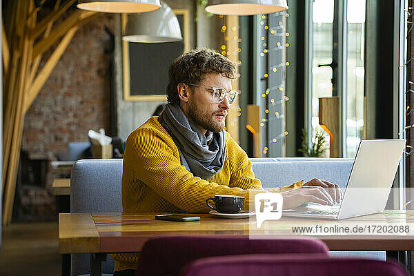 Männlicher Besitzer arbeitet am Laptop  während er im Café sitzt