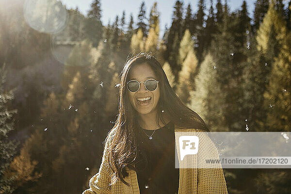 Junge Frau mit Sonnenbrille  die lächelnd im Wald steht