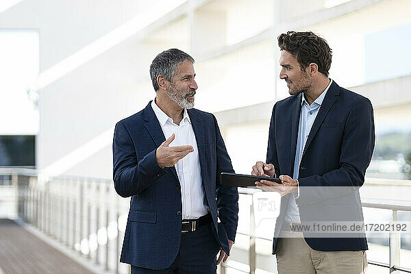 Business people discussing over digital tablet while standing at office building terrace
