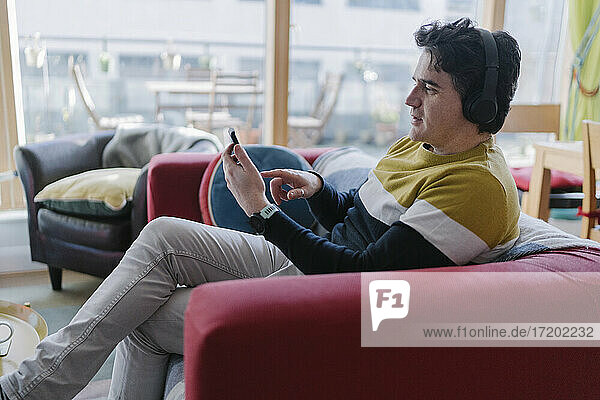 Man using smart phone while listening music through wireless headphones at home