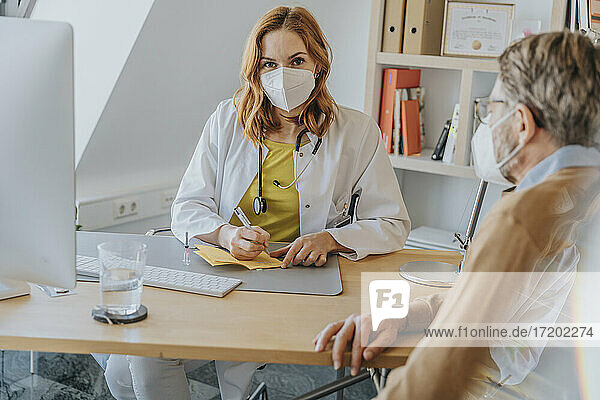 Mitarbeiter des Gesundheitswesens mit Gesichtsschutzmaske  der im Büro sitzend den Impfpass eines Patienten unterzeichnet