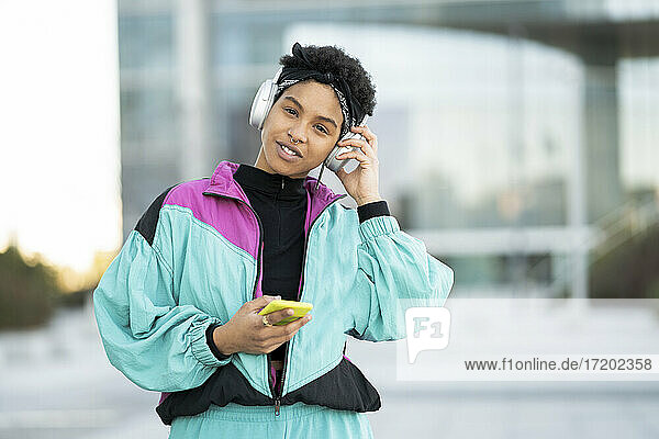 Funky young woman listening music through headphones in city