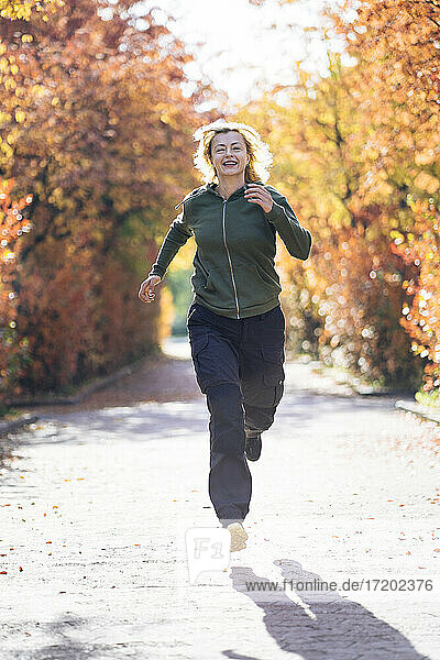 Cheerful mature woman running in park on sunny day