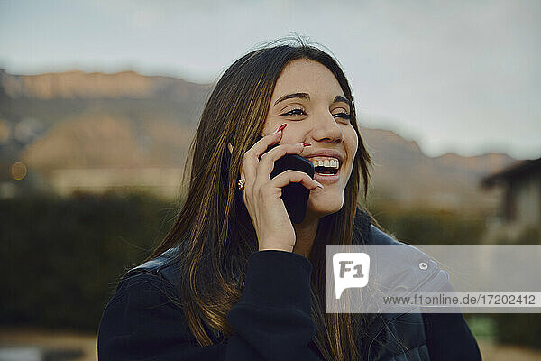 Lachende schöne Frau  die mit einem Smartphone spricht  mit Bergen im Hintergrund