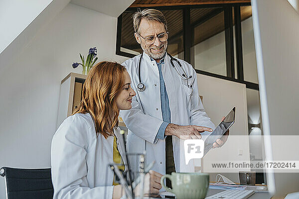 Male doctor showing digital tablet to coworker while standing at clinic