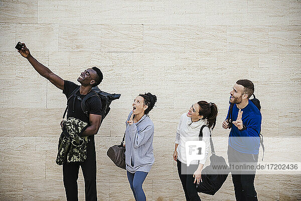 Cheerful athlete friends taking selfie through smart phone by wall
