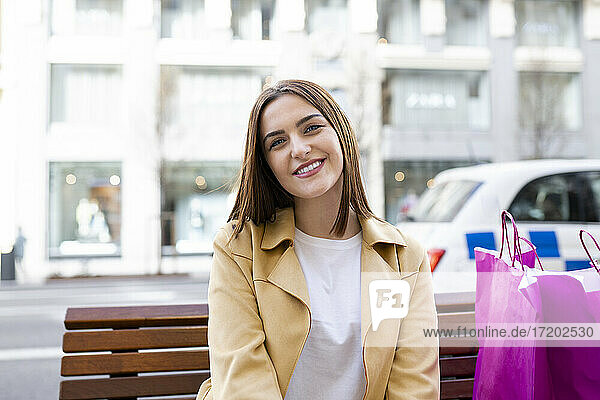 Schöne lächelnde Frau mit Einkaufstüten auf einer Bank sitzend