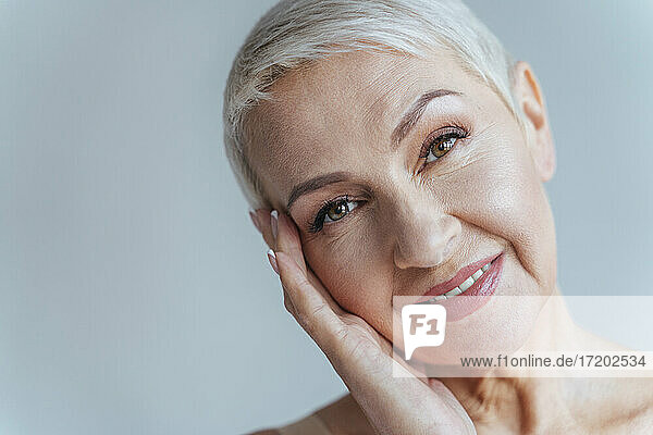 Ältere Frau lächelt im Stehen vor grauem Hintergrund