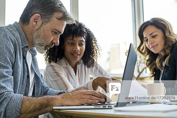 Männliche und weibliche Kollegen diskutieren über einen Laptop  während sie im Büro sitzen
