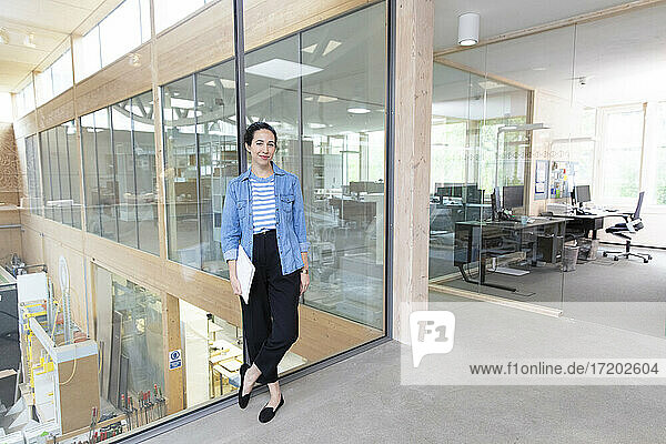 Businesswoman with document standing against glass wall in factory