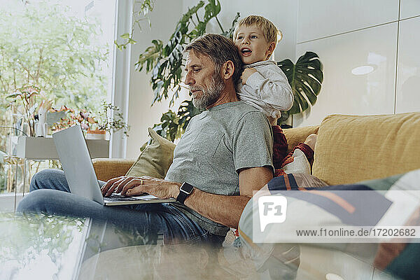 Playful boy leaning on father using laptop at home