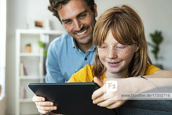 Vater und süße rothaarige Tochter schauen gemeinsam im Wohnzimmer auf ein Tablet