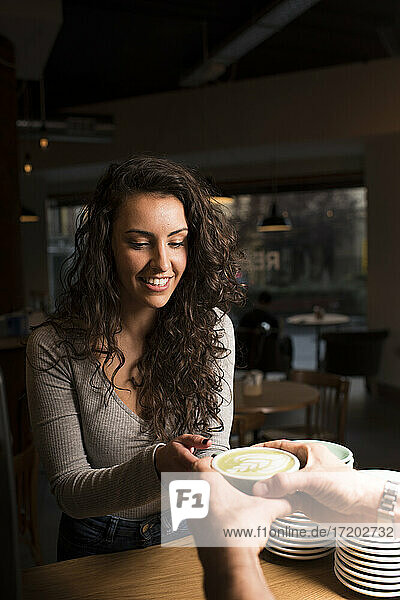 Smiling woman taking coffee cup at cafe