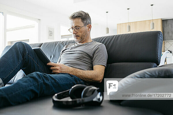 Mature man using digital tablet while sitting on sofa in living room