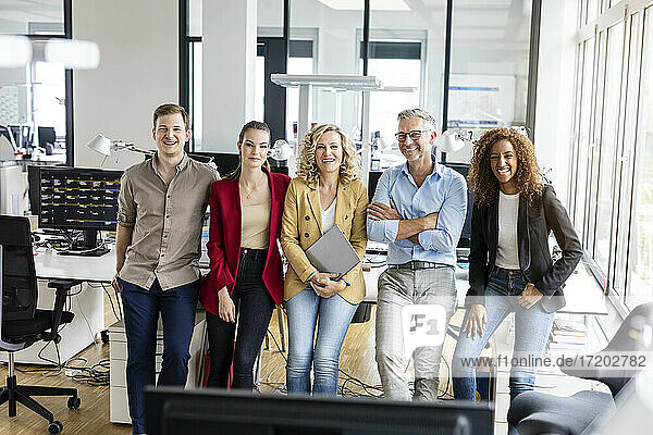 Lächelnde männliche und weibliche Unternehmer  die sich auf einen Schreibtisch im Büro stützen