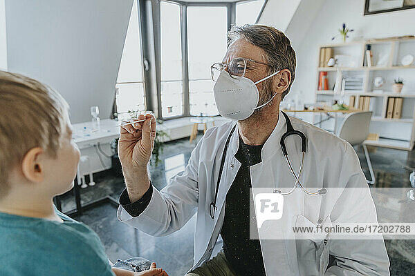 Männlich  mit Gesichtsschutzmaske  Kinderarzt  der einen Nasenabstrich bei einem Jungen macht  während er in der Klinik steht