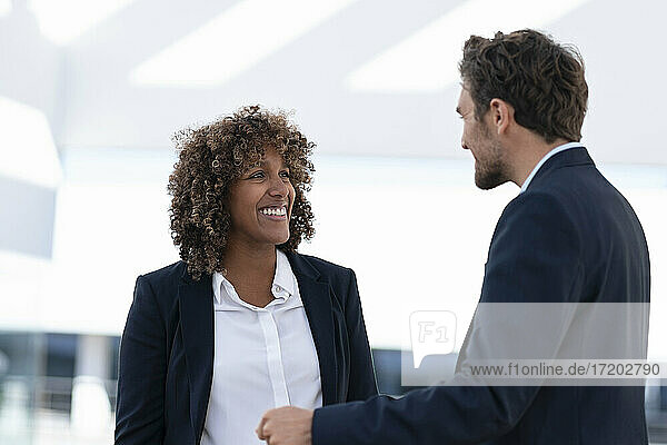 Lächelnde Geschäftsfrau  die einen Kollegen ansieht  während sie im Freien steht
