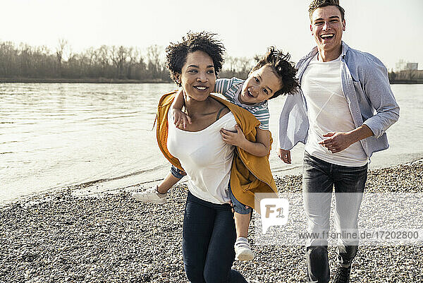 Junge Frau nimmt Jungen beim Laufen am Seeufer huckepack