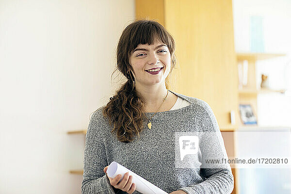 Lächelnde Frau mit Papier in der Hand im Büro stehend