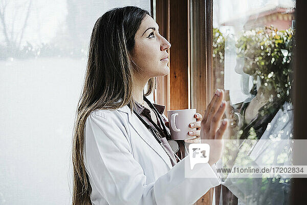 Nachdenkliche Ärztin schaut beim Kaffee durch das Fenster