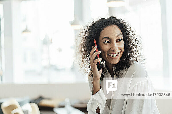 Smiling businesswoman talking on mobile phone while sitting at cafe
