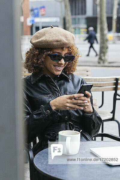 Fashionable teenage girl using mobile phone while sitting at sidewalk cafe