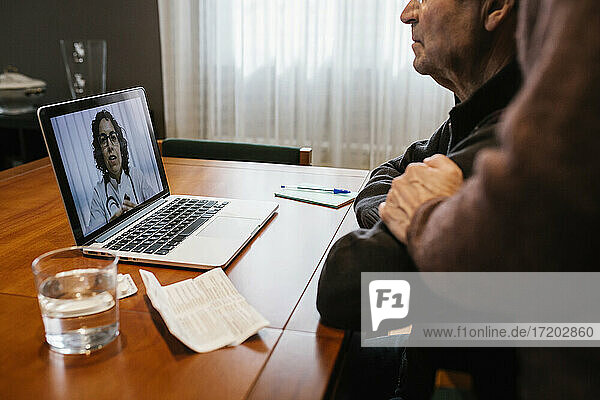 Ein älterer Mann und eine Sozialarbeiterin bei einer Online-Konsultation mit einer Ärztin zu Hause während COVID-19