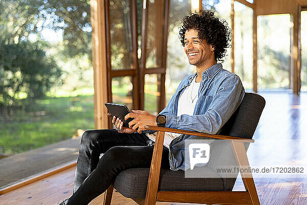 Lächelnder Mann  der ein digitales Tablet benutzt  während er im Vorgarten sitzt
