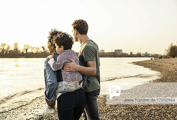 Junge Frau nimmt Jungen huckepack  während sie mit einem Mann am Seeufer spazieren geht
