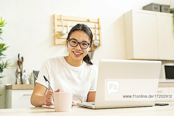 Frau lächelt  während sie zu Hause am Laptop sitzt