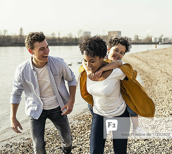 Happy man running with woman piggybacking boy by lake