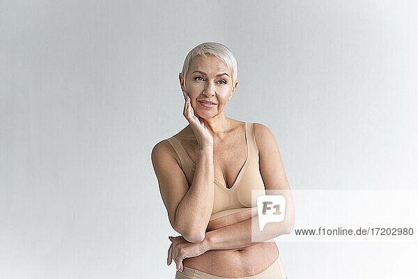 Nachdenkliche ältere Frau  die wegschaut  während sie vor einem grauen Hintergrund steht