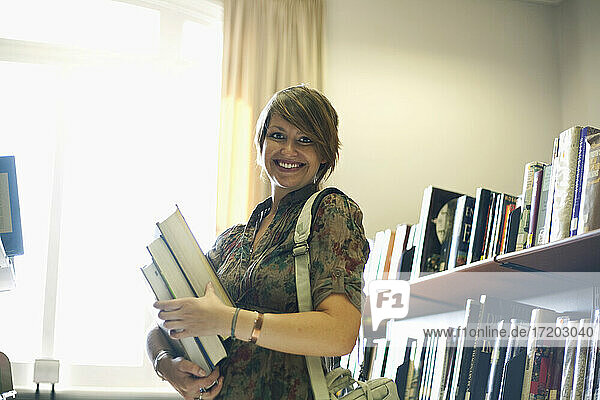 Lächelnde junge Frau mit Büchern in der Bibliothek