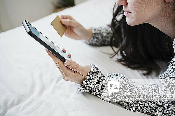 Frau mit Kreditkarte beim Online-Einkauf über das Mobiltelefon  während sie zu Hause auf dem Bett liegt