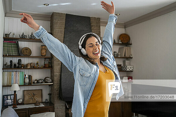 Fröhliche Frau mit Kopfhörern  die im Wohnzimmer stehend Musik genießt