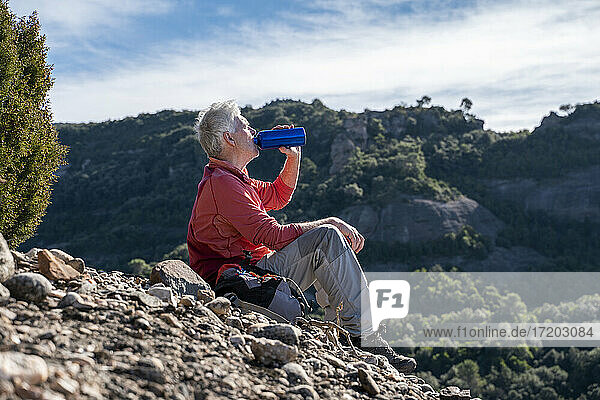 Male hiker drinking water while sitting on mountain at Sant Llorenc del Munt i l'Obac  Catalonia  Spain